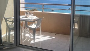 Un balcon avec une table et des chaises, une vue sur la mer et un navire à l’horizon.