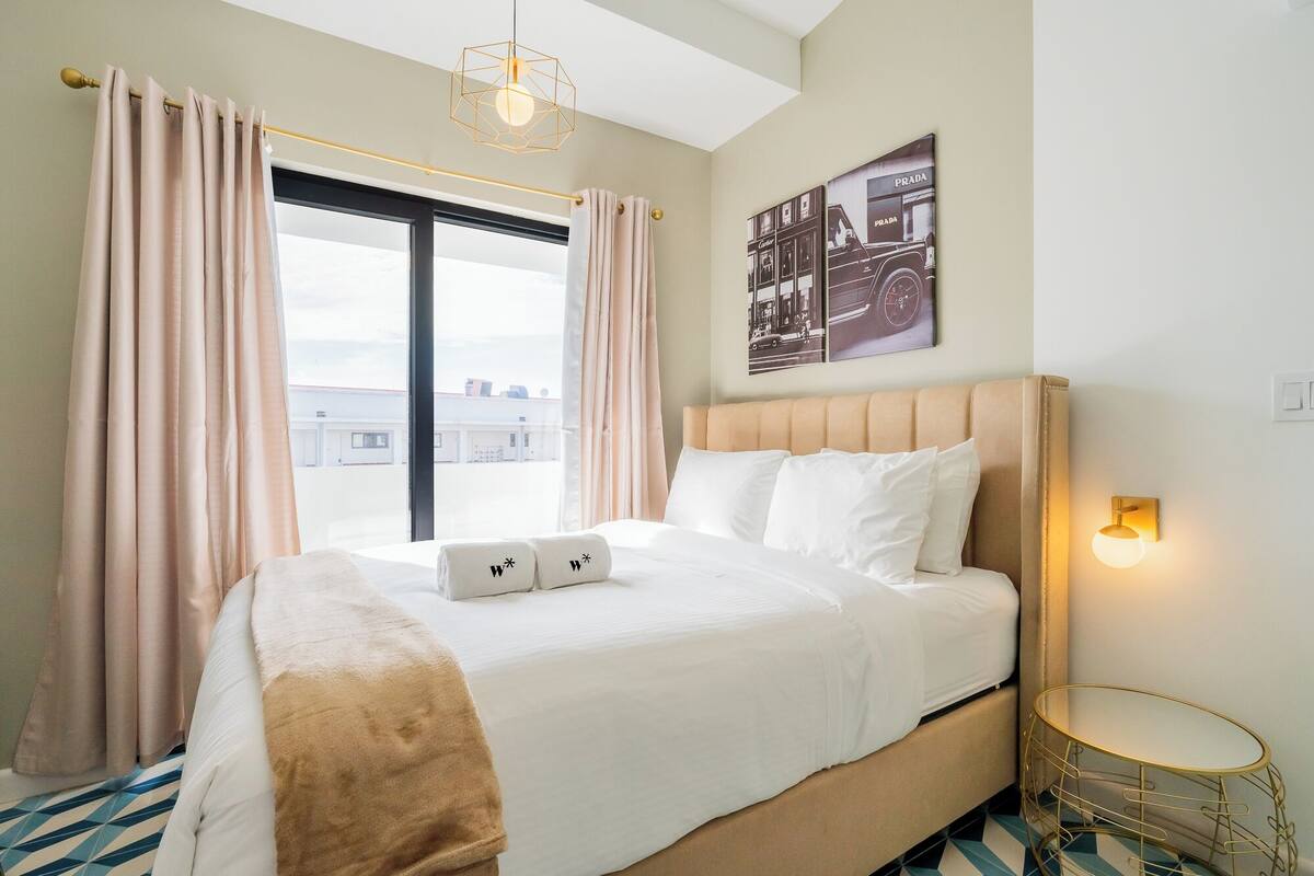 Ein Hotelzimmer mit einem großen Bett, einem Vorhangfenster, einer Wandleuchte und einem kleinen runden Tisch.