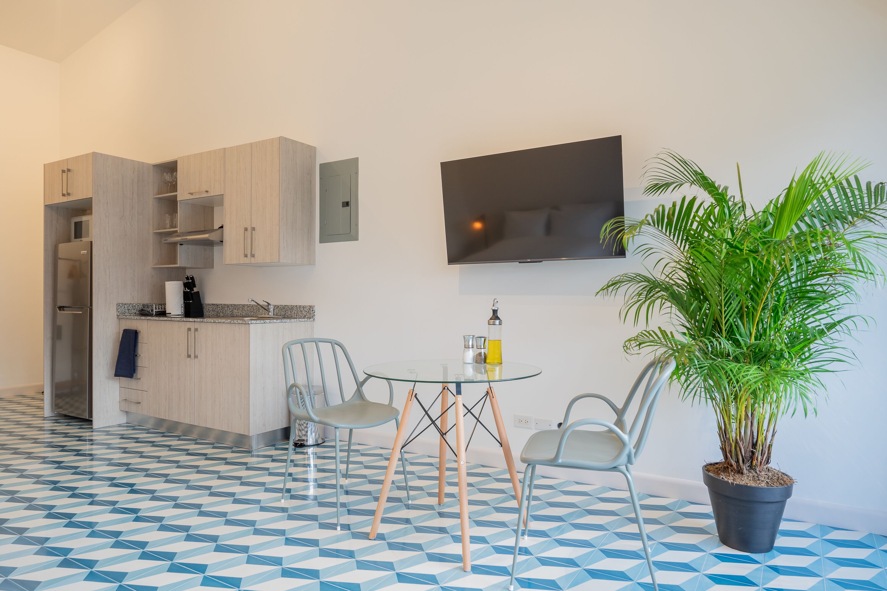 Una cocina moderna con electrodomésticos integrados, una zona de comedor con mesa de vidrio y una planta en maceta.