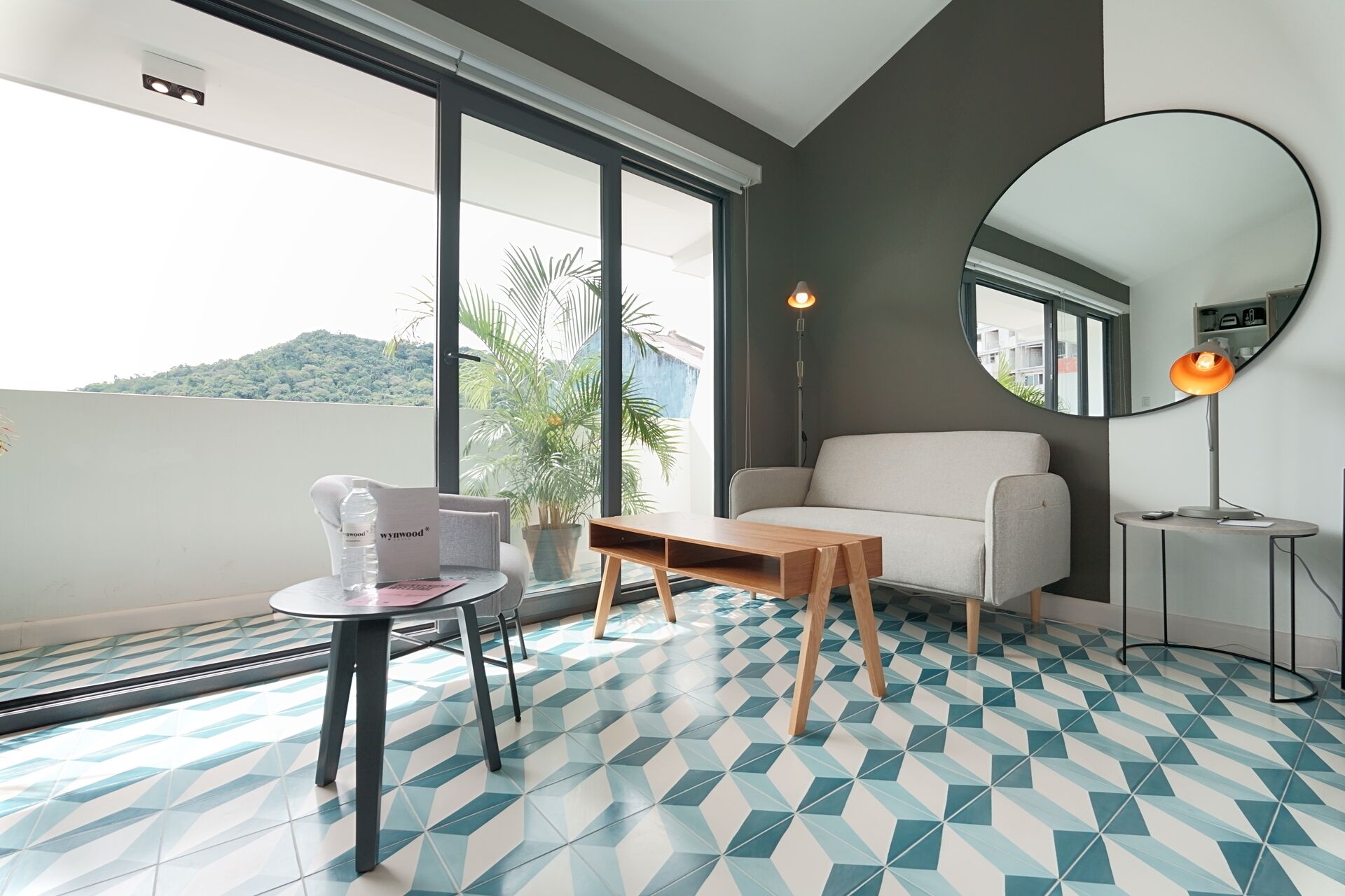 A modern room with a sofa, a small table, and a chair. There is a large window with a view of greenery outside.