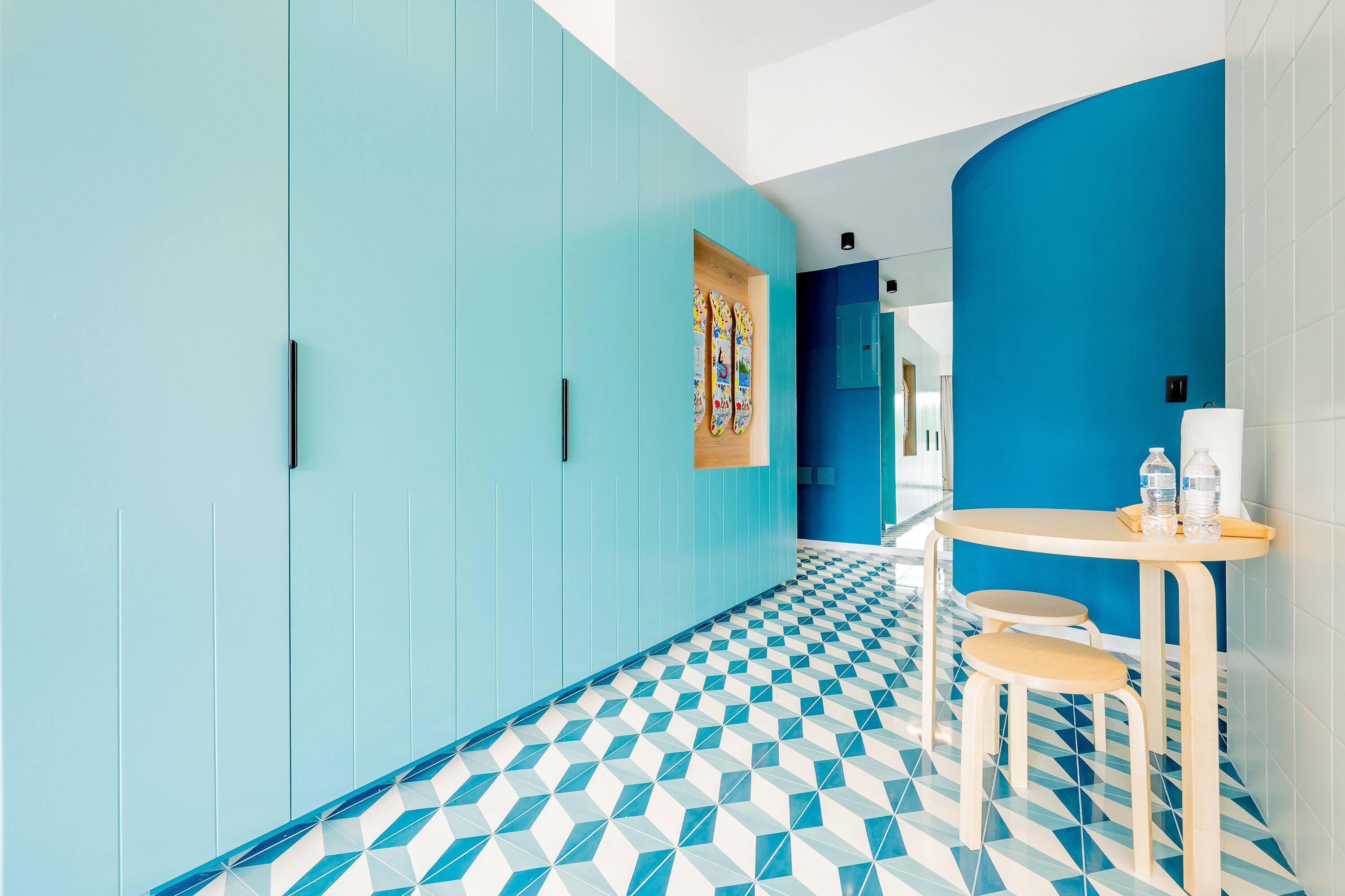 A hallway with teal walls and a geometric patterned floor, leading to a seating area with a table and chairs.