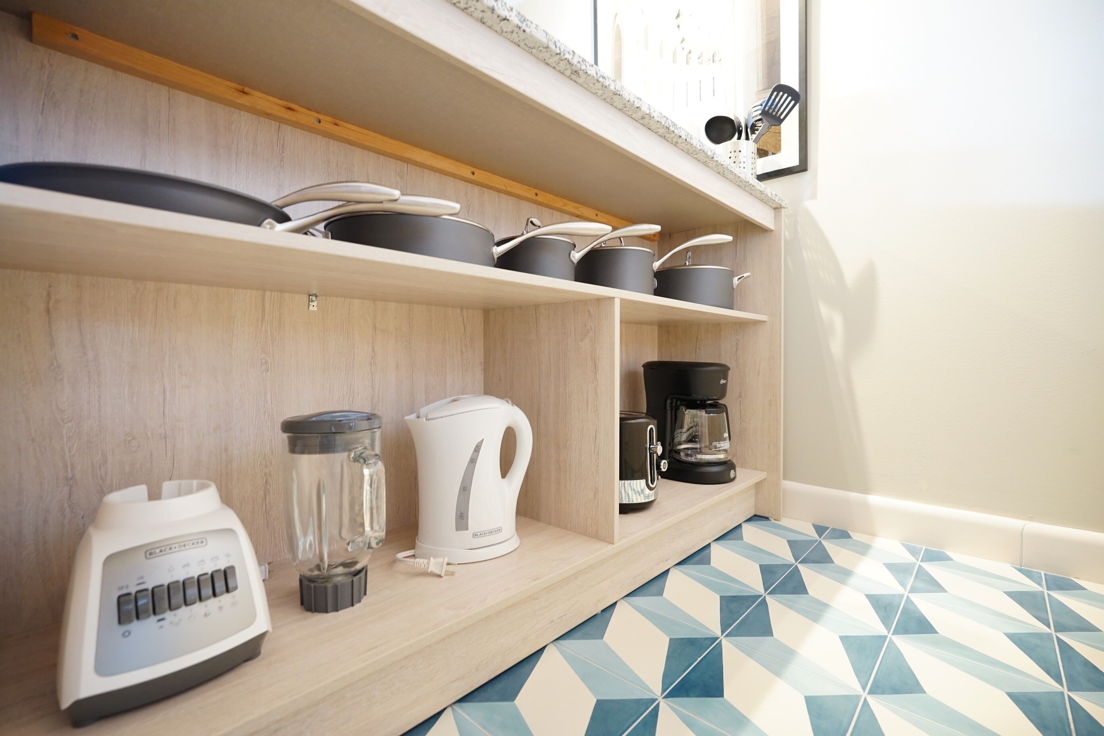 Een keuken met houten planken waarop pannen, potten, een koffiezetapparaat, een waterkoker en een blender staan.