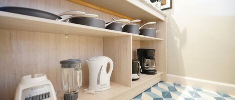 Een keuken met houten planken waarop pannen, potten, een koffiezetapparaat, een waterkoker en een blender staan.
