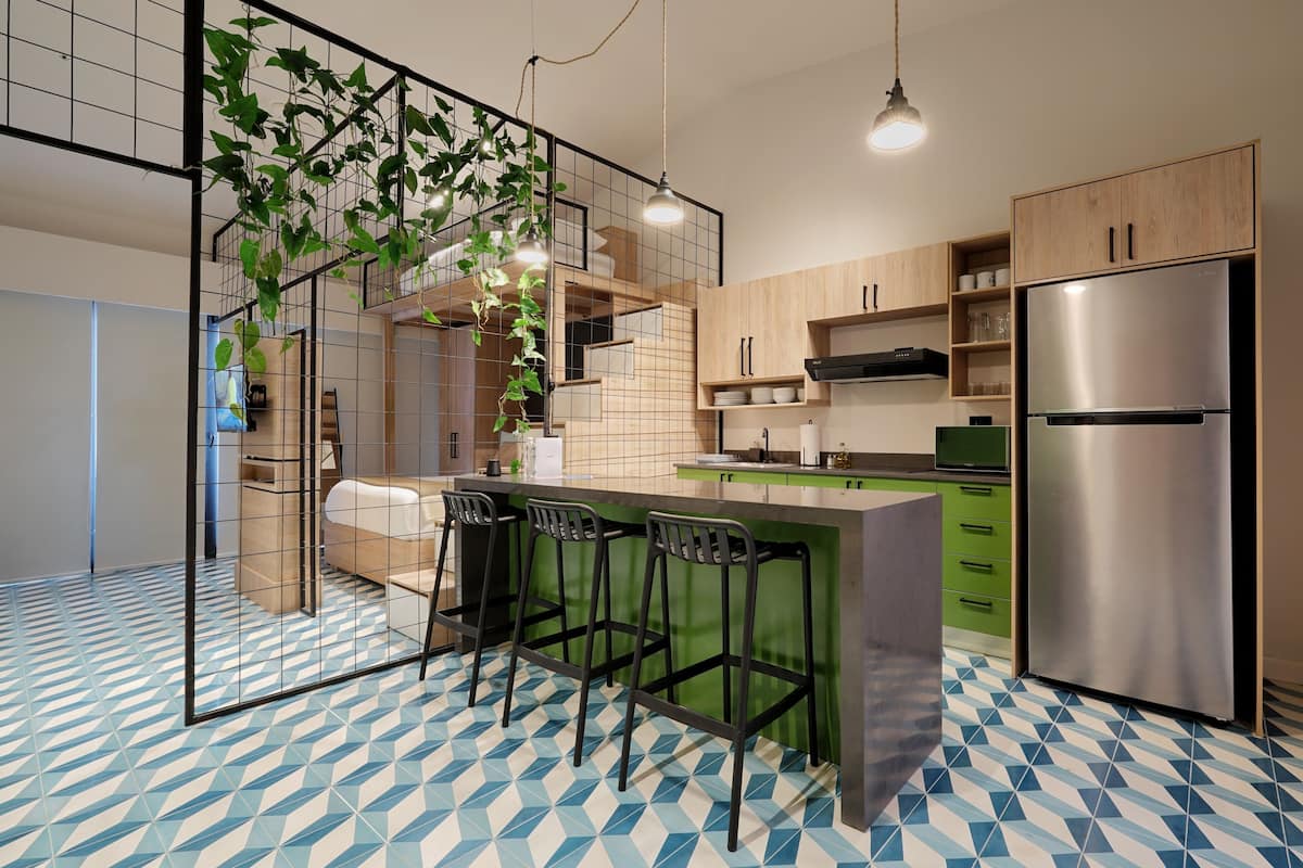 Eine moderne Küche mit Bar, grünen Barhocker, einem Edelstahlkühlschrank und einem gemusterten Boden.