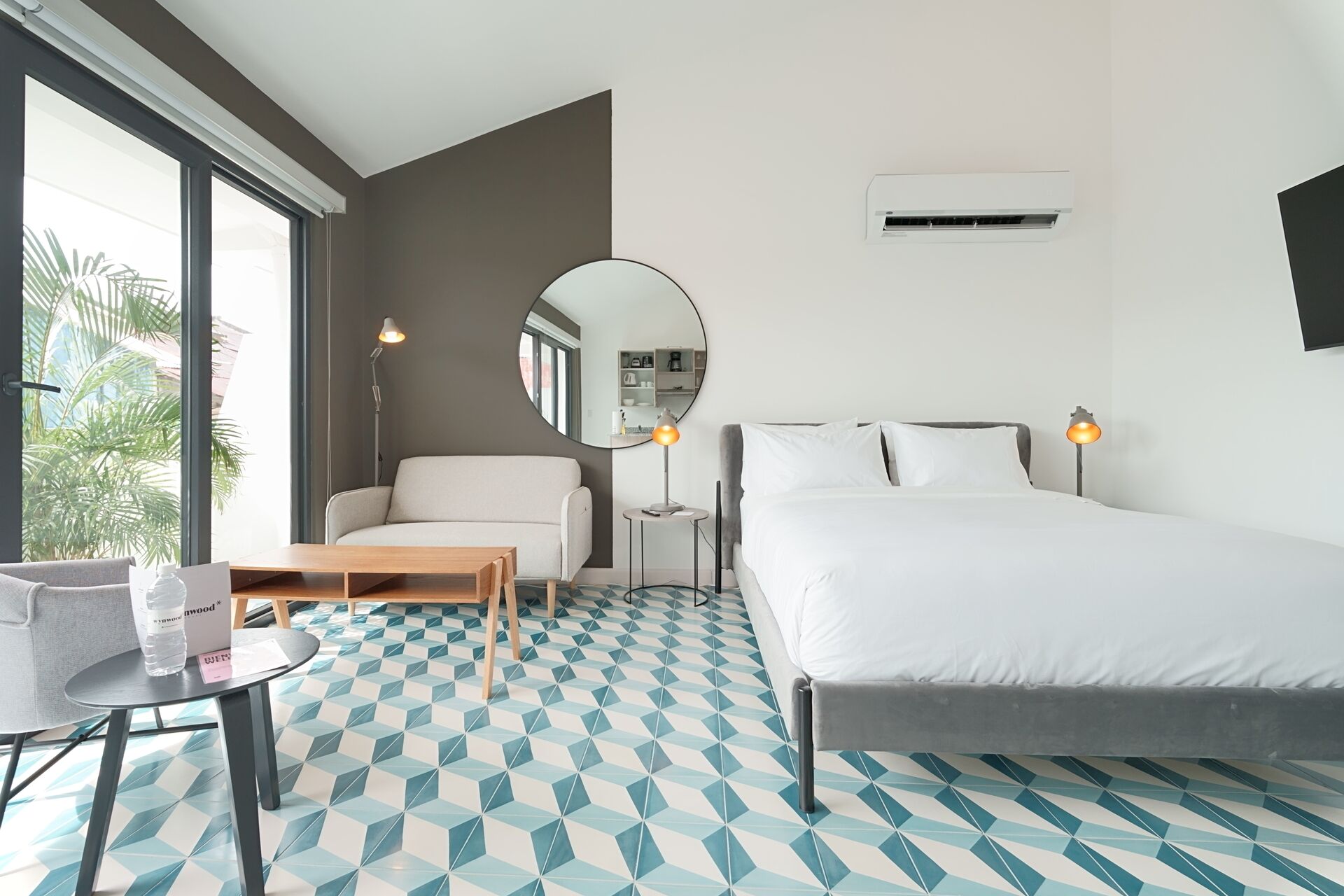 Una habitación de hotel con una cama, un sofá, un espejo redondo, una mesita y una silla.
