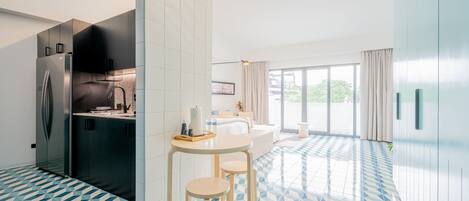 A modern kitchen with a built-in refrigerator, a dining area with a round table and two stools, and a large window providing natural light.