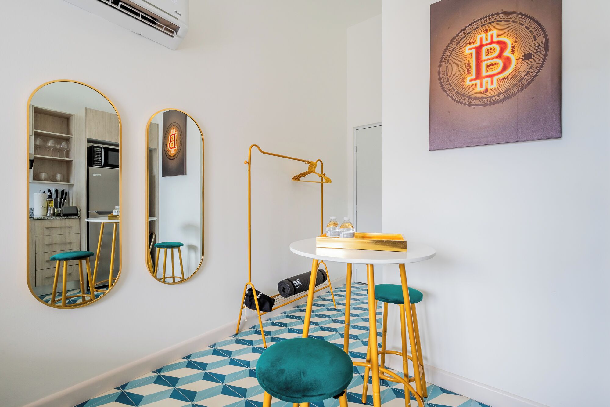 Ein modernes Zimmer mit Küchenzeile, einem runden Spiegel, einem Schreibtisch mit Hocker und einem Kunstwerk zum Thema Bitcoin.