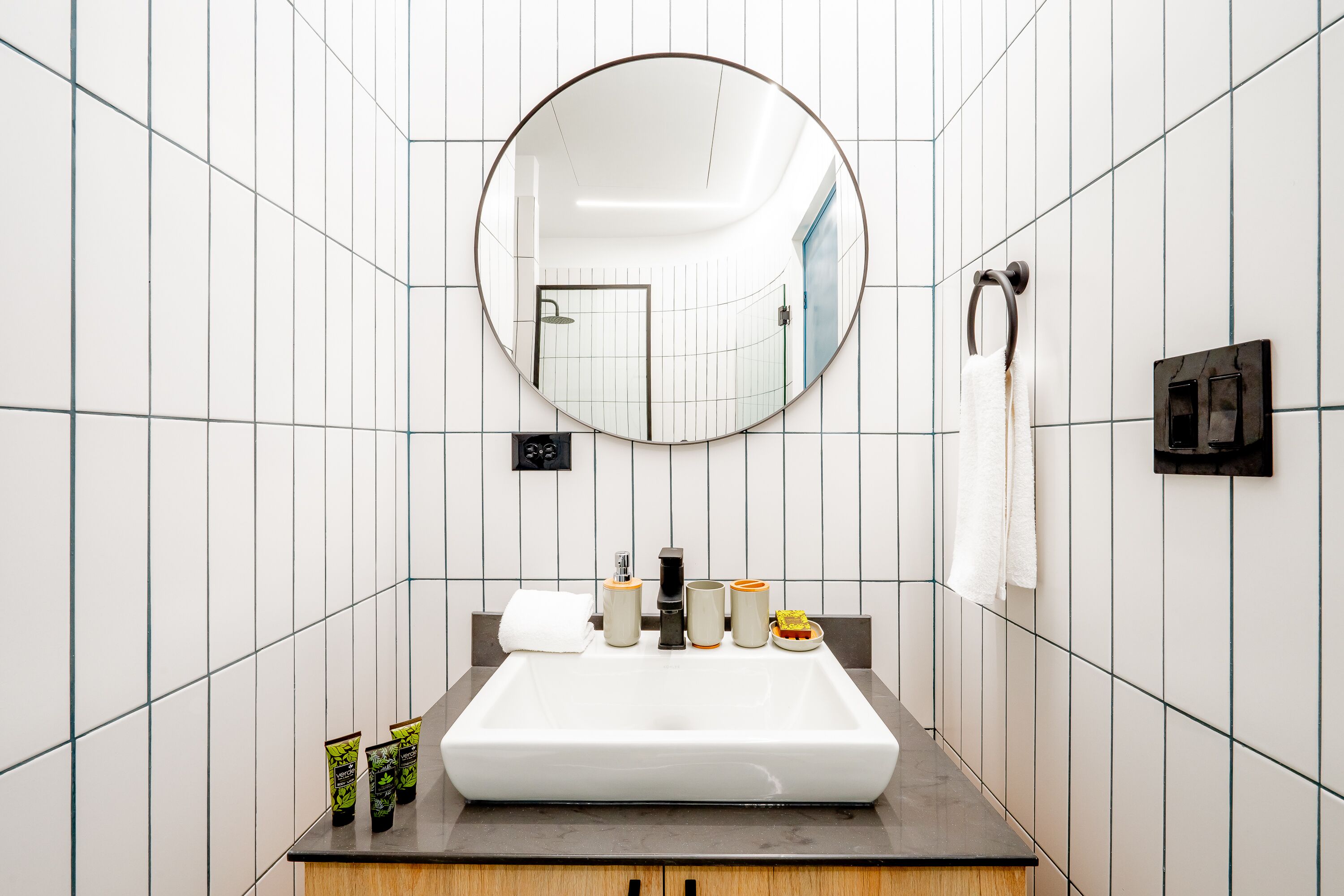 A modern bathroom with a large mirror, white tiles, and a wooden vanity.