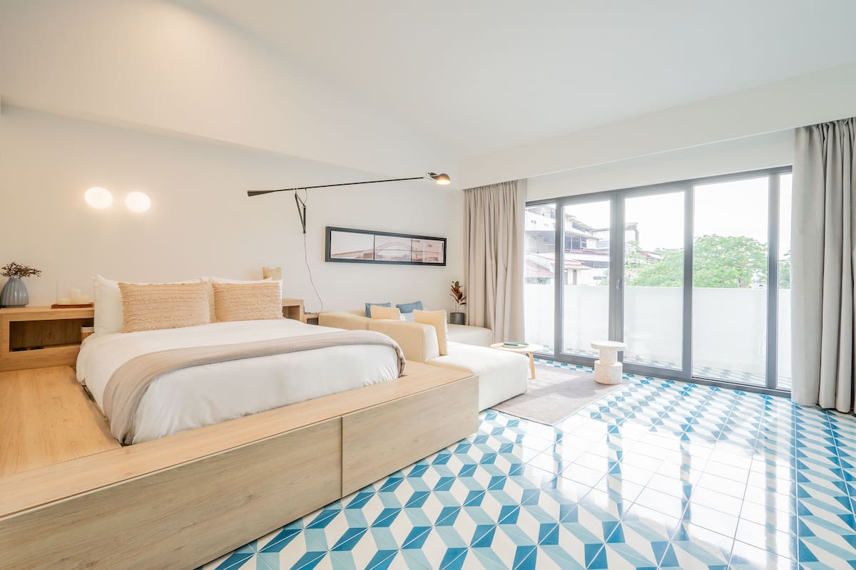 Ein modernes Schlafzimmer mit einem großen Bett, einer Couch, einem Schreibtisch und Blick ins Freie.