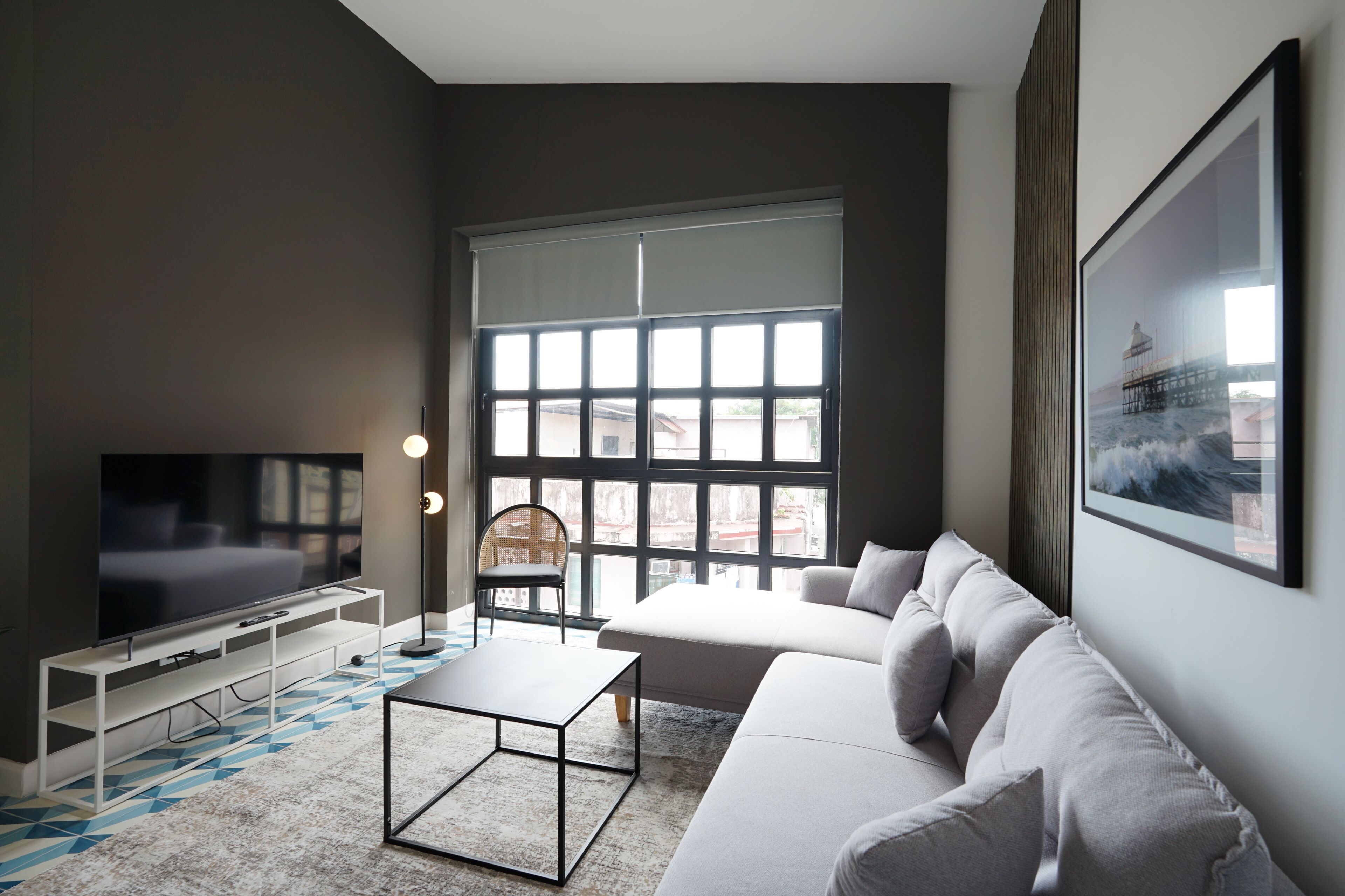 Una sala de estar moderna con un televisor grande, un sofá, una mesa de centro y una ventana con persianas.