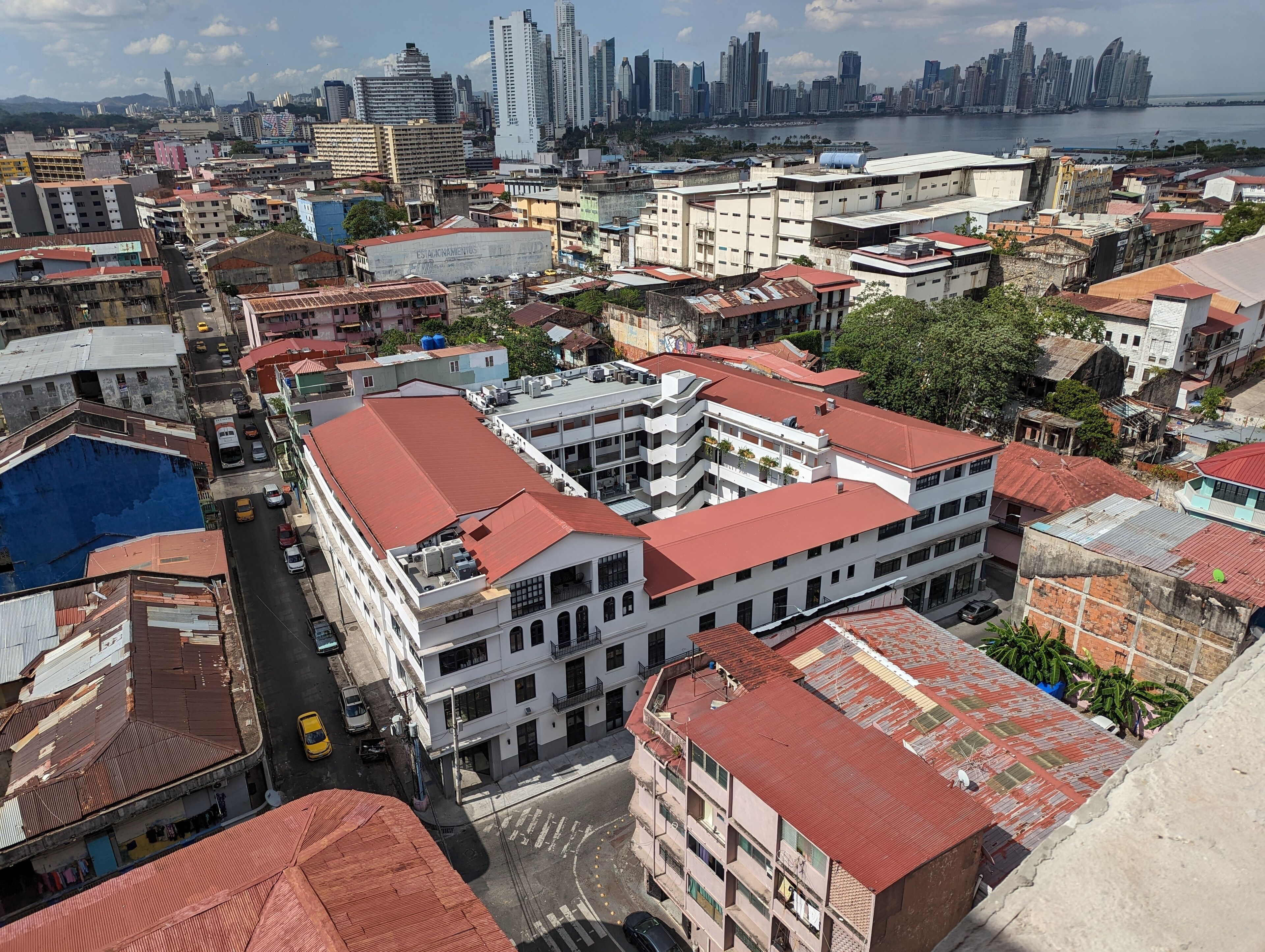 Un edificio alto con varios pisos, techo rojo y vista del horizonte urbano al fondo.