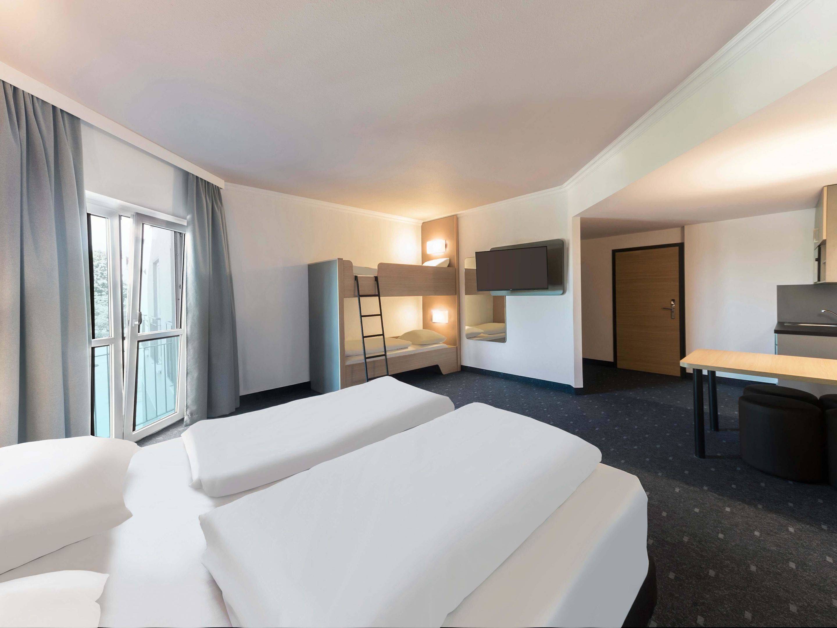 A hotel room with two beds, a desk, a TV, and a window with curtains.