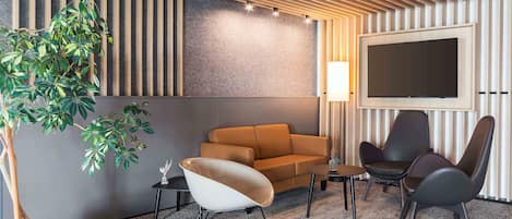 A modern living room with a sofa, two chairs, a coffee table, a TV mounted on the wall, and a potted plant.