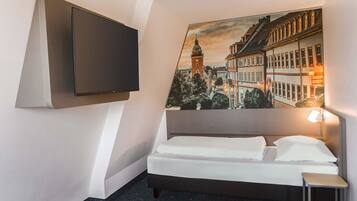 Een hotelkamer met een bed, een aan de muur bevestigde televisie, een klein nachtkastje en een schilderij van een stadsgezicht.