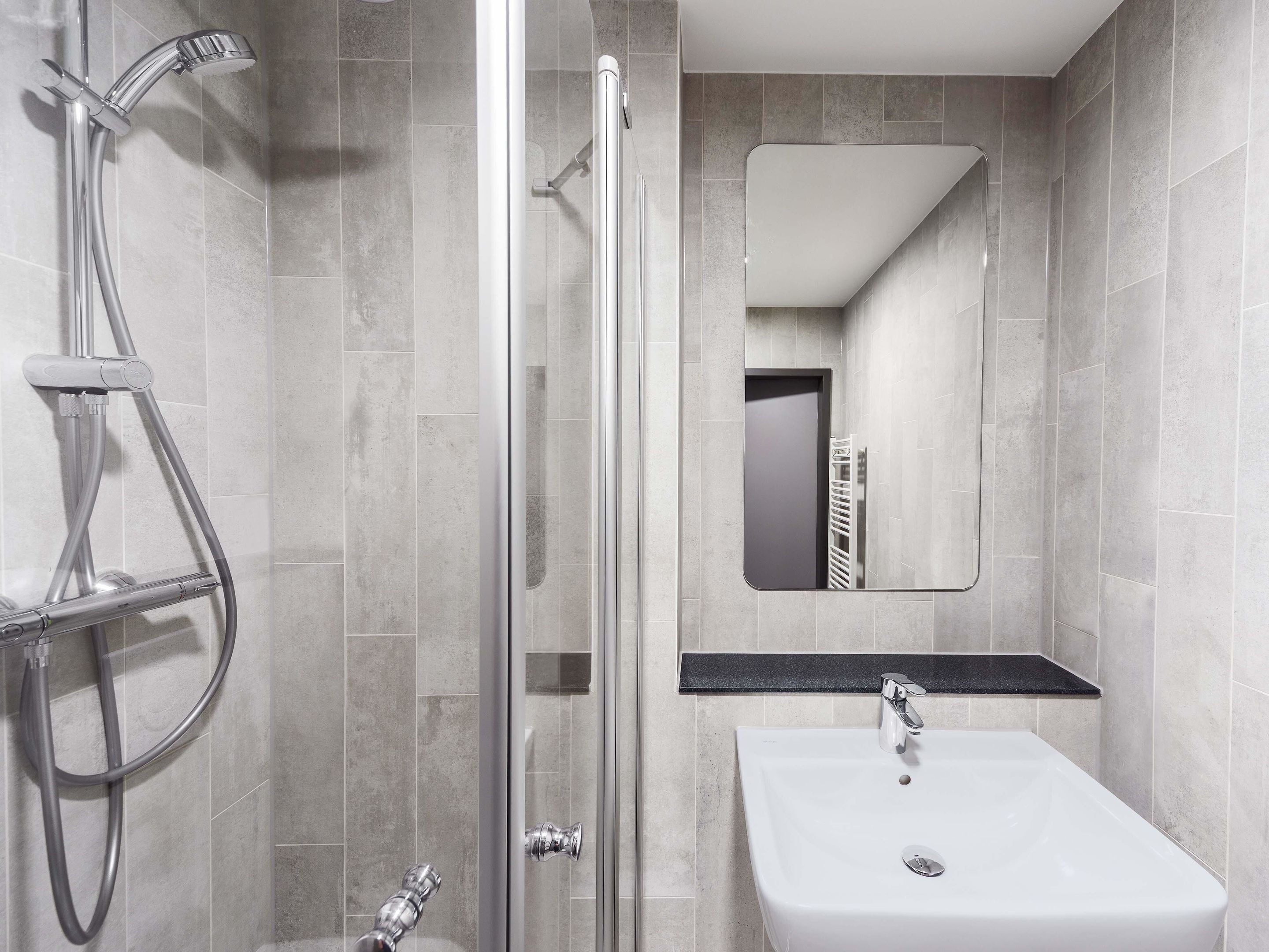 Un baño moderno con ducha de vidrio, lavamanos blanco y espejo sobre el lavamanos.