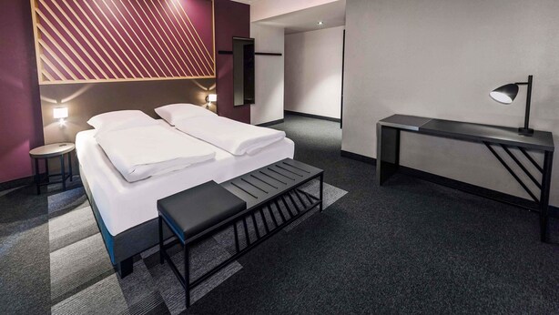 Una habitación de hotel moderna con una cama, mesitas de noche, un escritorio y un banco.
