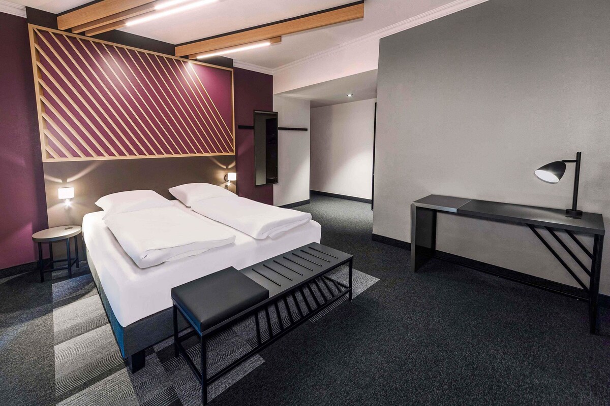 Una habitación de hotel moderna con una cama, mesitas de noche, un escritorio y un banco.
