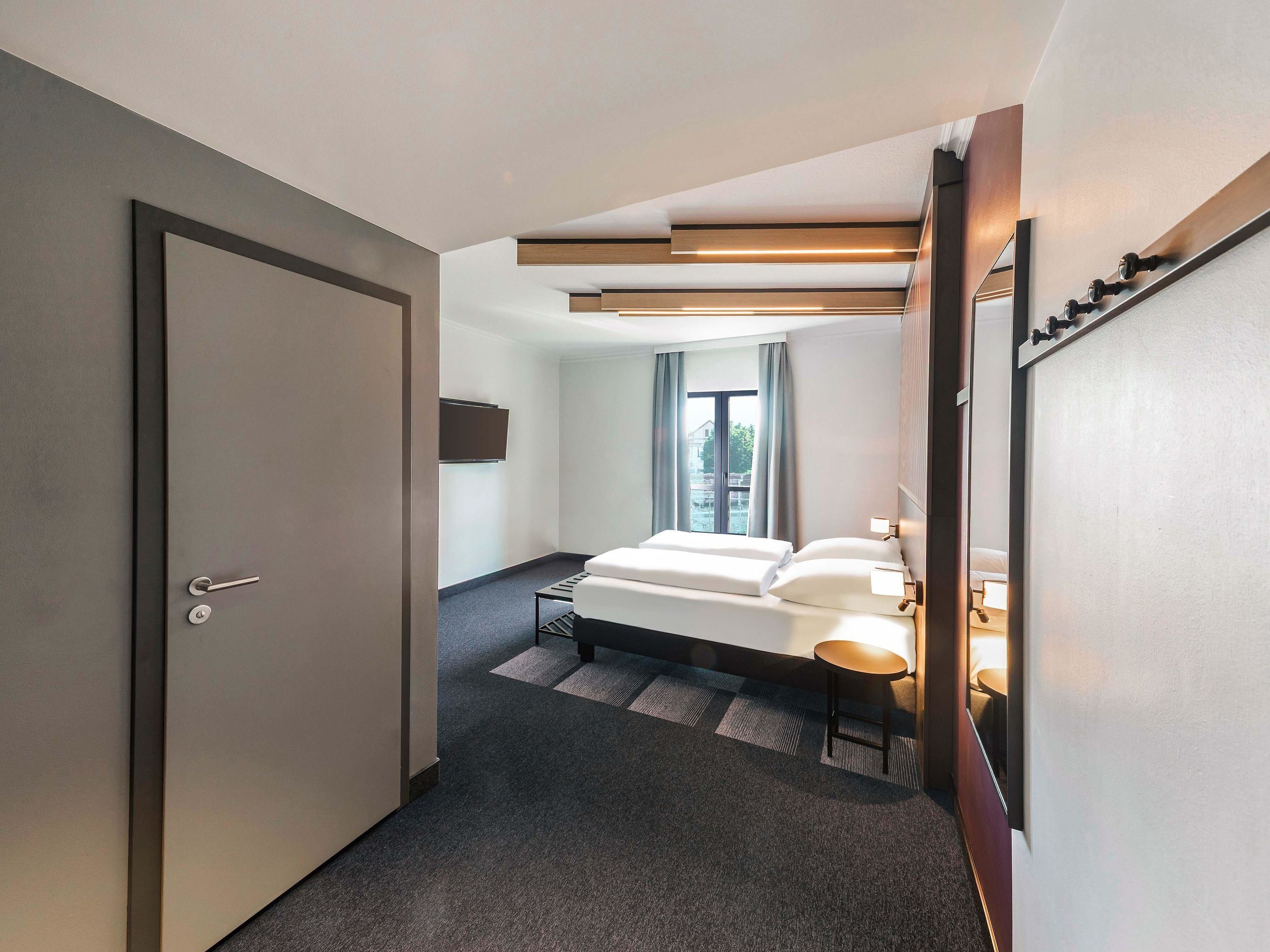 Ein modernes Hotelzimmer mit Bett, Nachttisch und Blick ins Freie.