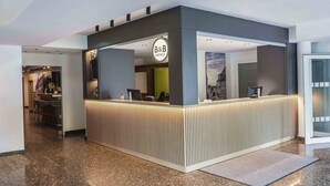 Un mostrador de recepción moderno con un letrero de 'B&B', una zona de bar y vistas a la ciudad.