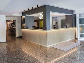 Un mostrador de recepción moderno con un letrero de 'B&B', una zona de bar y vistas a la ciudad.