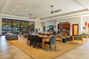 A hotel lobby with a reception desk, guest registration area, dining area with a large wooden table and chairs, and a seating area with sofas and armchairs. - Oceanfront Corner Condo with Panoramic Views in Kahana (Lahaina)