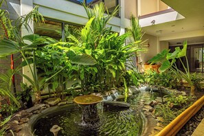 An indoor garden with a water feature, surrounded by various tropical plants.