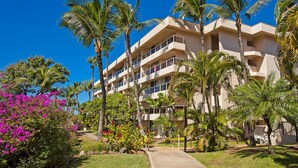 A multi-story hotel with balconies, surrounded by palm trees and vibrant bougainvillea. - Maui Banyan Kihei condo w/ large lanai and ocean views, summer deal (Kihei)