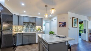 A modern kitchen with grey cabinets, a large island, and pendant lighting. - Maui Banyan Kihei condo w/ large lanai and ocean views, summer deal (Kihei)