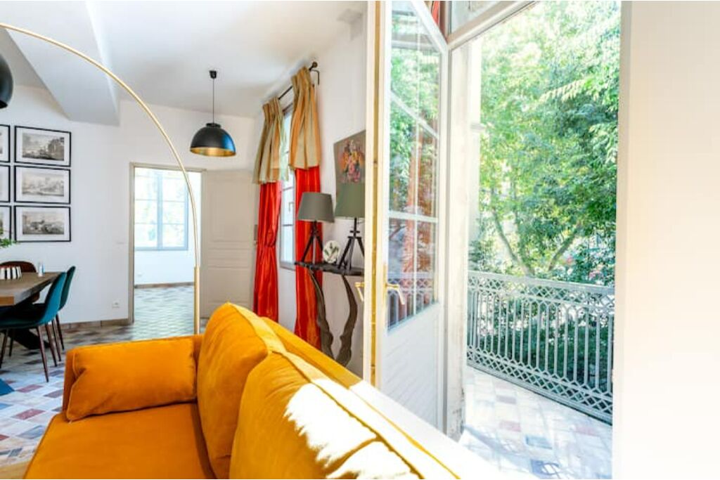 A bright room with a yellow sofa, a dining table, and a large window with a view of greenery.