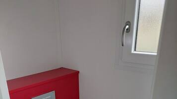 A small, compact bathroom with a red accent wall, a white toilet, and a window.