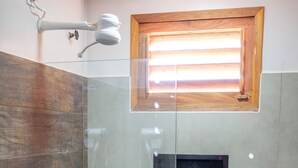 A modern bathroom with a glass-enclosed shower, a wooden-framed window, and a built-in sink.