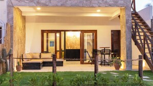 A two-story building with a stone facade, a balcony with a wooden railing, and a seating area with a sofa and chairs.