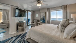 A spacious bedroom with a large bed, a ceiling fan, a TV, and a balcony with a view of the ocean. - Blue Ocean Front Escape (MYRTLE BEACH)
