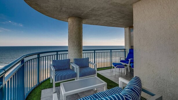 A balcony with a view of the ocean, featuring striped blue and white outdoor furniture and a white table. - Blue Ocean Front Escape (MYRTLE BEACH)