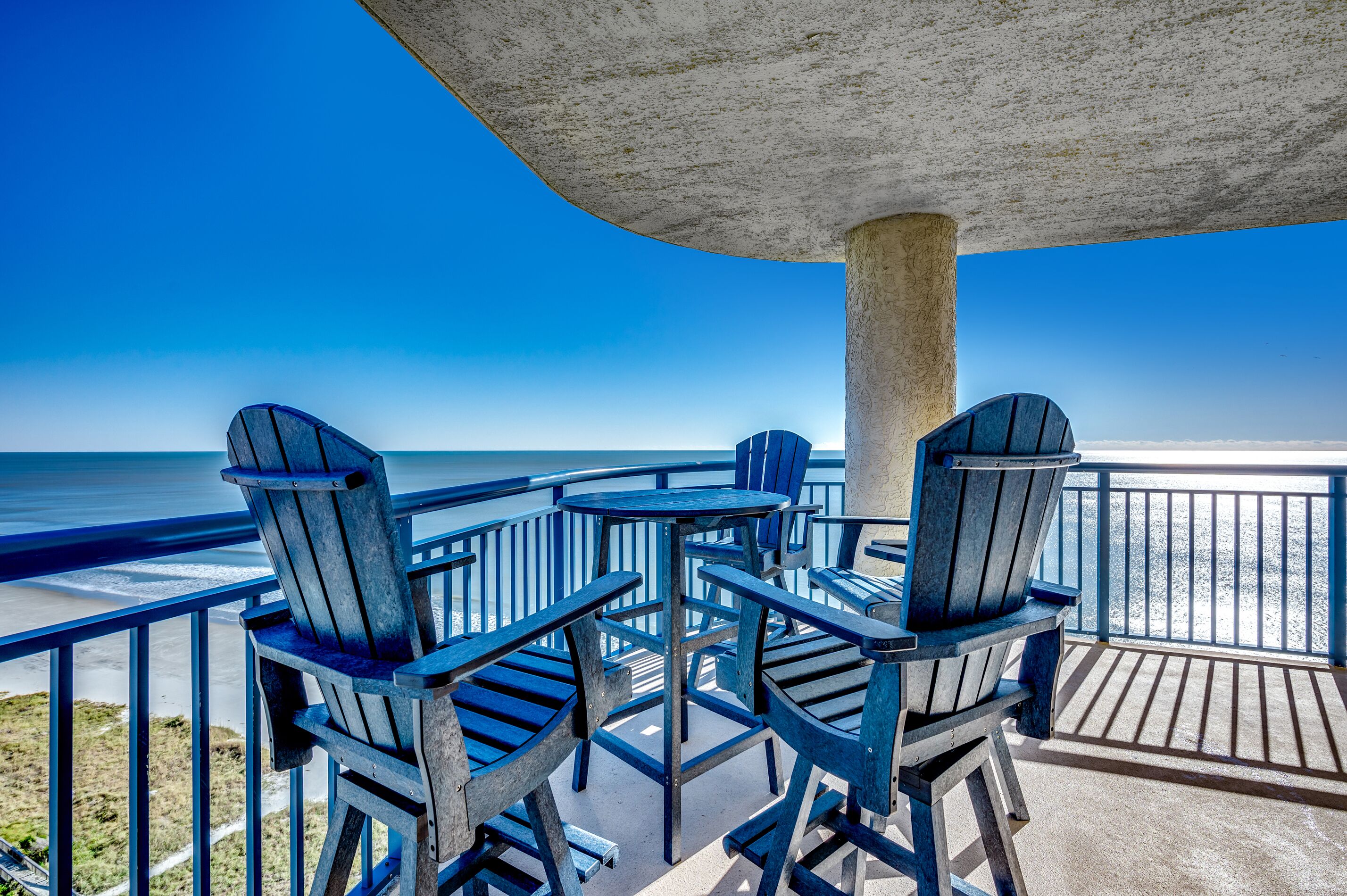 A wooden deck with chairs and a table overlooking the beach.