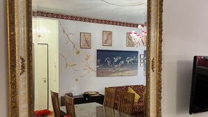 Un espace repas agrémenté d’un grand miroir, d’un lustre et d’un téléviseur fixé au mur.