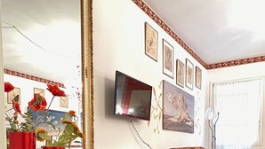 Un salon moderne avec un meuble de rangement noir pour les appareils électroniques, des vases rouges, un canapé agrémenté d’un coussin jaune et un téléviseur à écran plat fixé au mur.