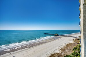 A beach with a pier extending into the ocean, sandy beach, and a building on the right. - Ocean Front Crown New Remodel (MYRTLE BEACH)