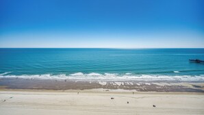 A beach with a pier extending into the ocean, sandy shore, and clear blue sky. - Ocean Front Crown New Remodel (MYRTLE BEACH)