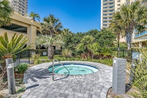 A circular pool with a metal ladder, surrounded by a brick patio and palm trees. - Ocean Front Slice of Heaven (MYRTLE BEACH)