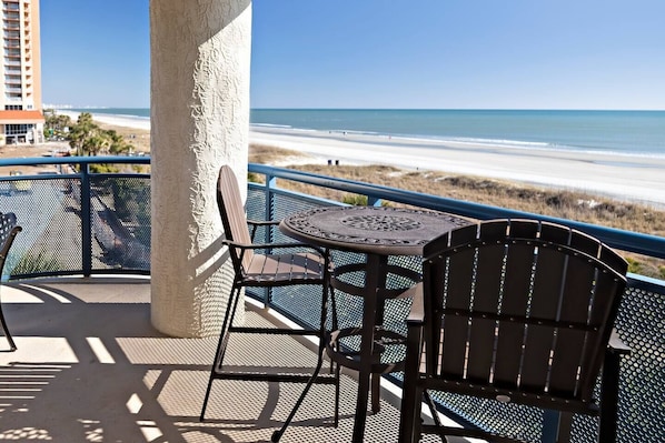 A balcony with a table and two chairs overlooking a beach. - Ocean Front Slice of Heaven (MYRTLE BEACH)