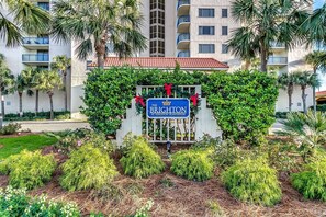 Une enseigne indiquant « The Brighton at Kingston Plantation », avec une entrée fermée par un portail, entourée d’un jardin paysager et de palmiers.