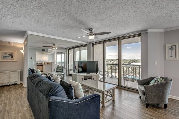 A spacious living area with a sofa, armchair, and a TV on a glass table. A ceiling fan and a balcony with a view are also visible. - The Getaway of Kingston Resort (MYRTLE BEACH)