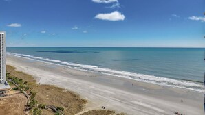A beach with a clear view of the ocean, a sandy shore, and a building with a sloped roof. - The Love Shack Myrtle Beach (Myrtle Beach)