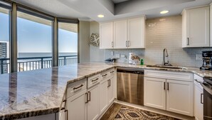 A modern kitchen with white cabinets, a stainless steel dishwasher, and a large window overlooking the ocean. - The Love Shack Myrtle Beach (Myrtle Beach)