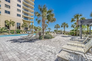 A hotel pool area with lounge chairs, palm trees, and a building with balconies. - The Love Shack Myrtle Beach (Myrtle Beach)