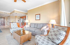 A living room with a sofa, two armchairs, a coffee table, and a kitchen in the background.