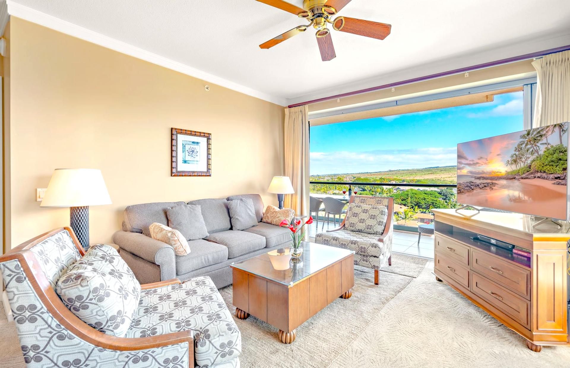 A hotel room with a sofa, two armchairs, a coffee table, a TV, and a balcony with a scenic view.