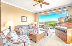 A hotel room with a sofa, two armchairs, a coffee table, a TV, and a balcony with a scenic view.