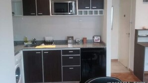 Ett kompakt kök med mörka skåp, en inbyggd mikrovågsugn och en tvättmaskin.